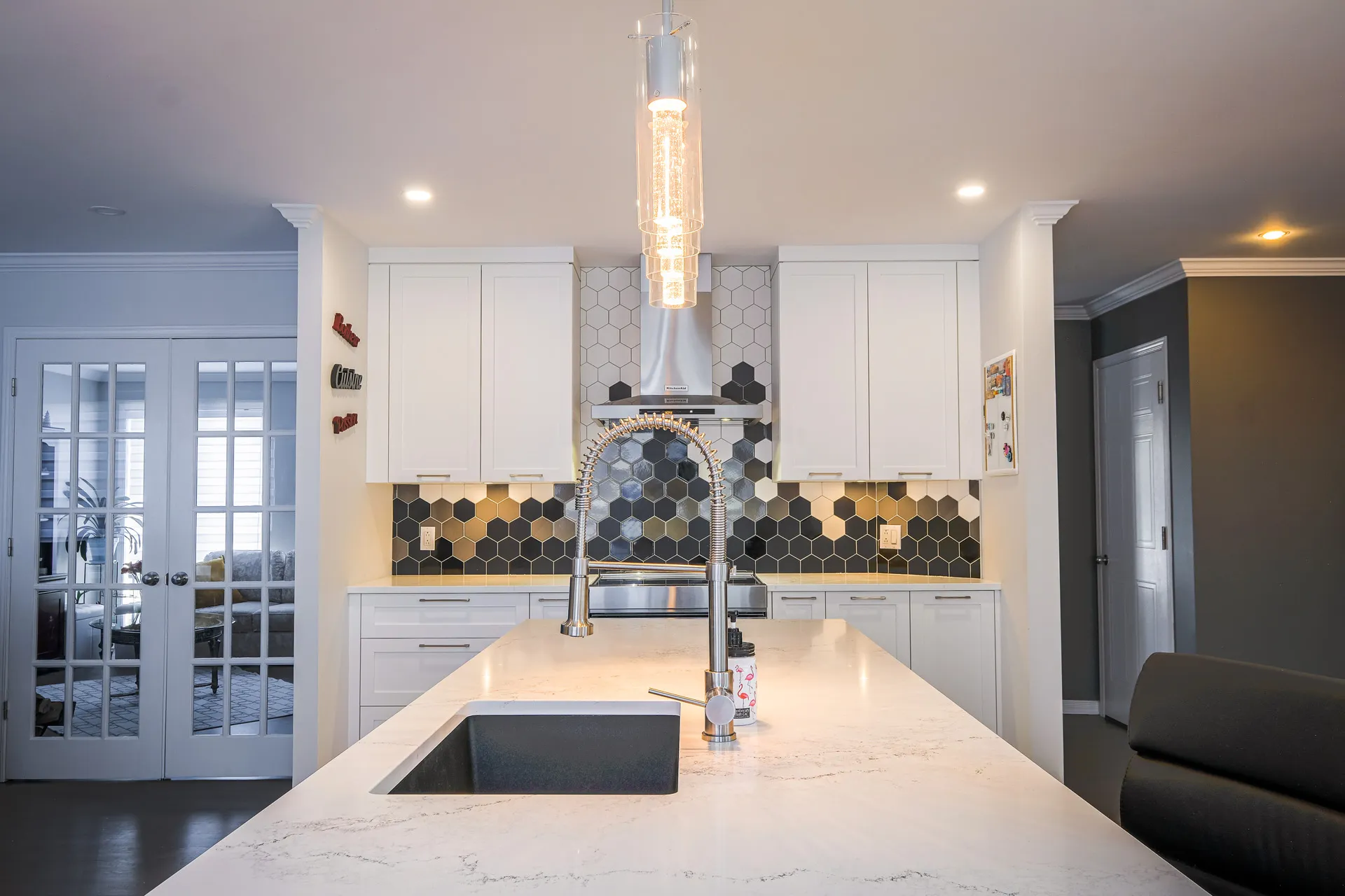 Modern Landry kitchen with white cabinets, marble countertop, central island, black hexagonal backsplash and chrome