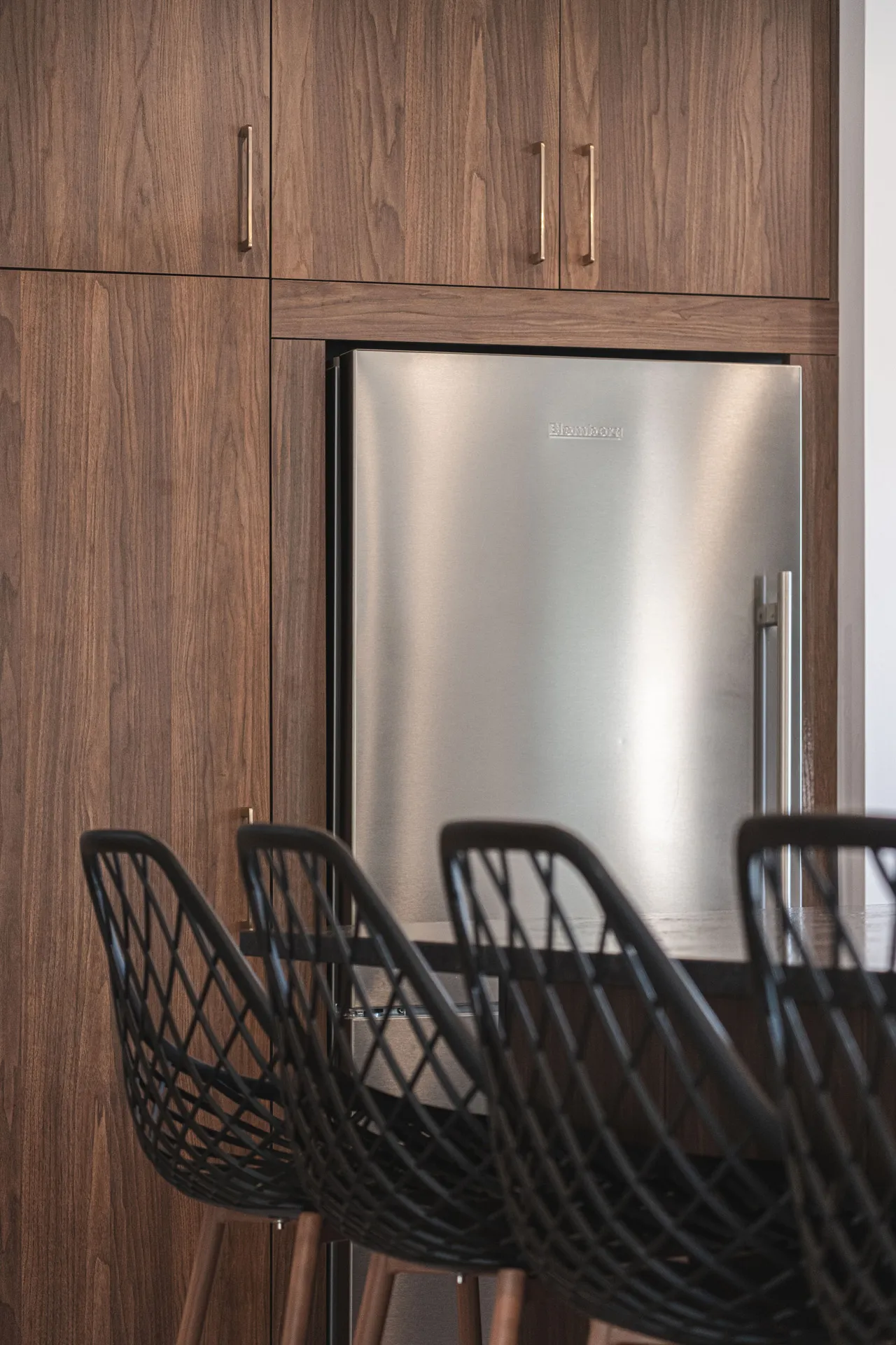 Modern Montreal kitchen: walnut cabinets, stainless steel refrigerator, black designer chairs, Denis project Menuitech