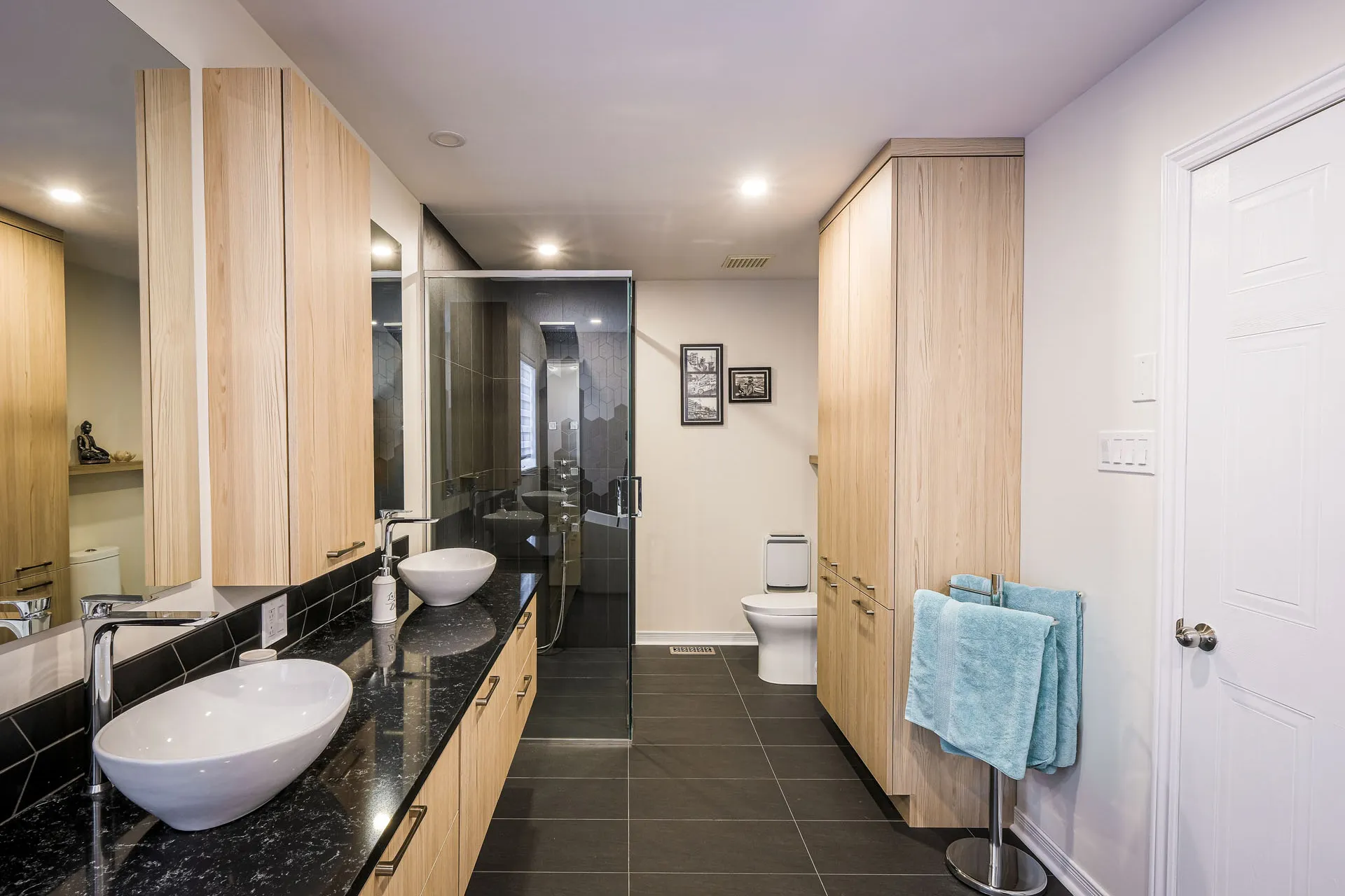 Landry bathroom: light wood cabinets, black granite countertop, dual white sinks, glass shower enclosure, grey tile