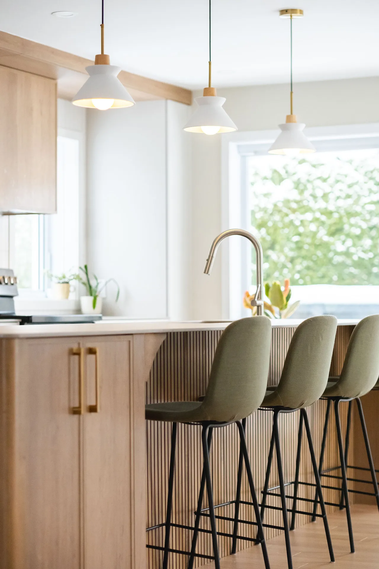 Cuisine moderne Blainville : armoires bois clair, comptoir blanc, îlot avec tabourets beige, luminaires suspendus blancs