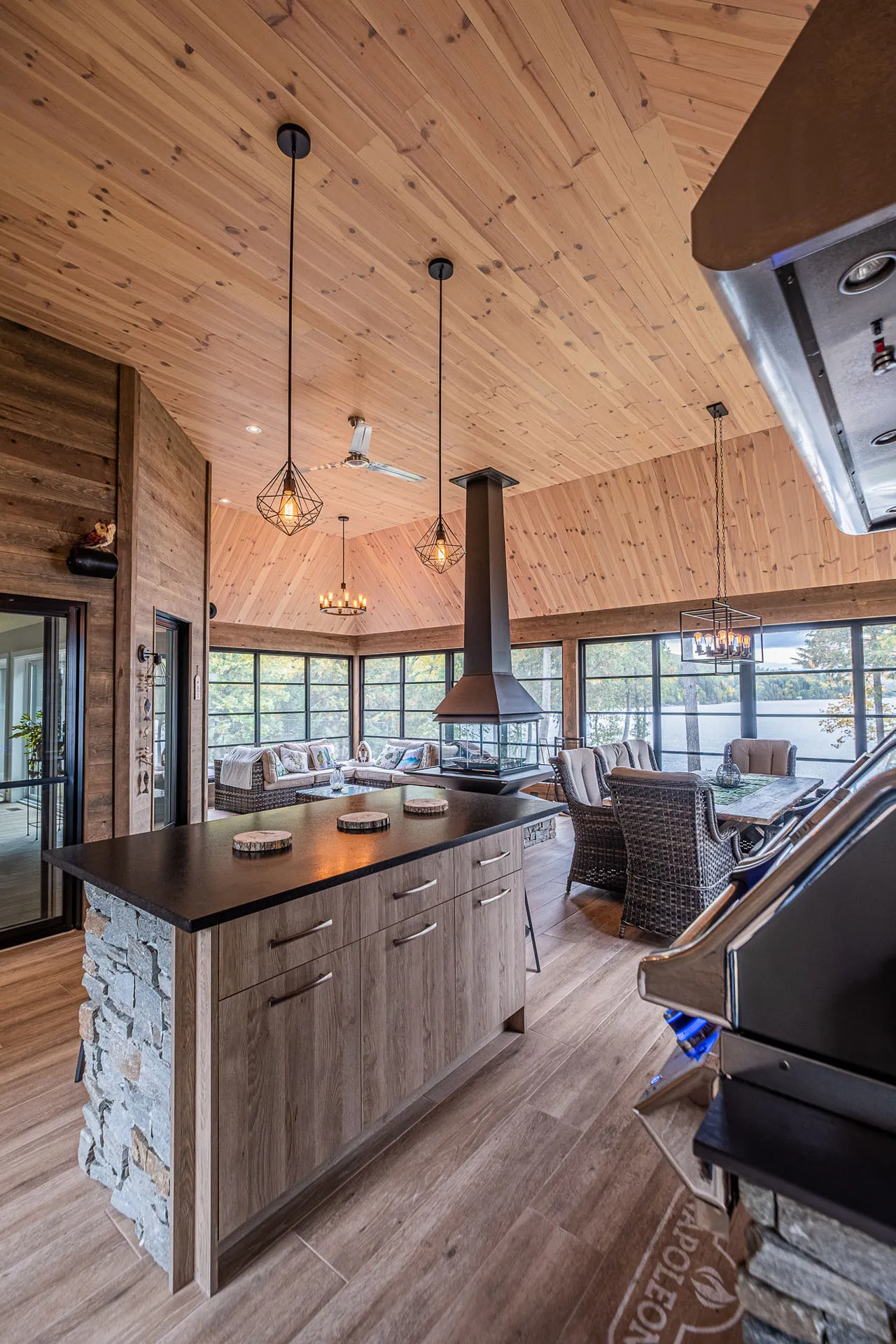 Open kitchen light wood island, black countertop, gray cabinetry, pendant lights, central fireplace, picture windows
