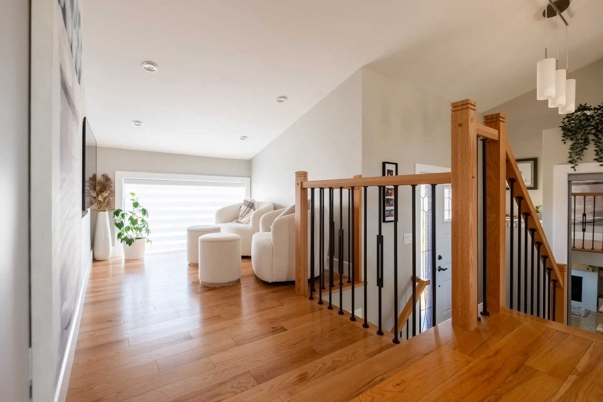 Escalier bois avec rampe noire dans loft moderne, plancher chêne, murs blancs et luminaires suspendus