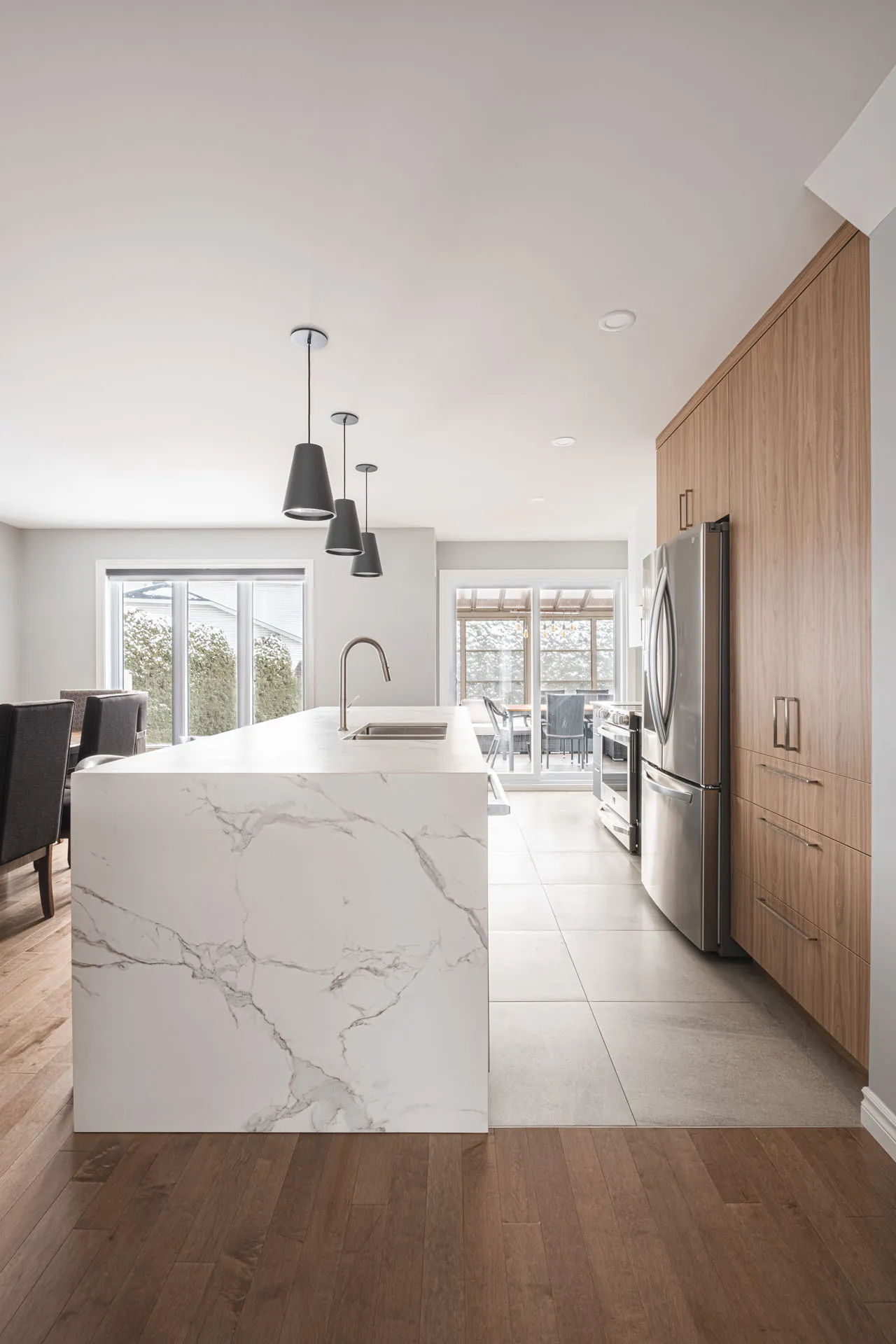Modern Landry D'Amours kitchen with white marble island, natural wood cabinets, stainless steel appliances and black pendant lights