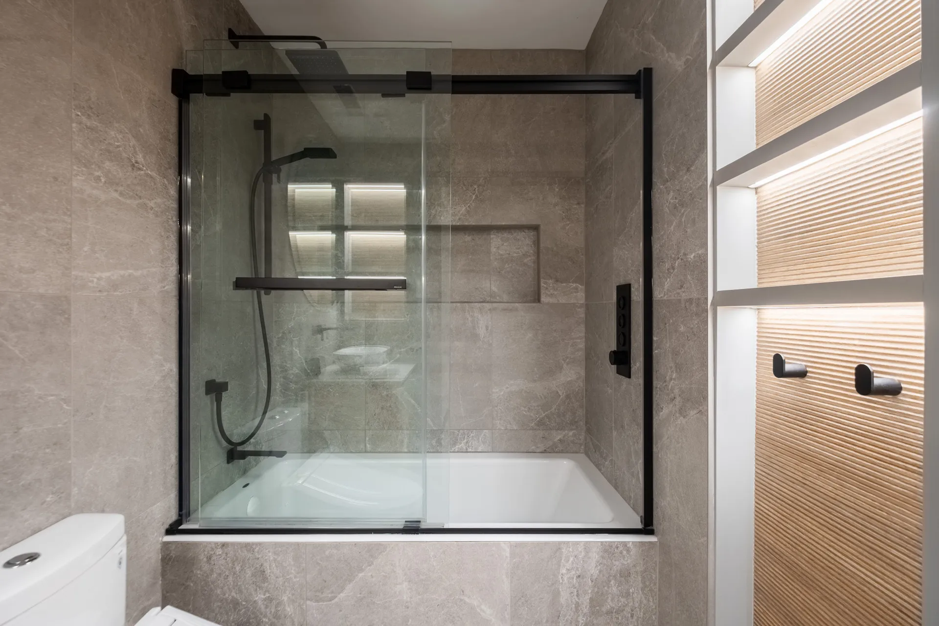 Salle de bain moderne avec douche intégrée à baignoire, carrelage gris taupe, armoire bois clair et quincaillerie noire