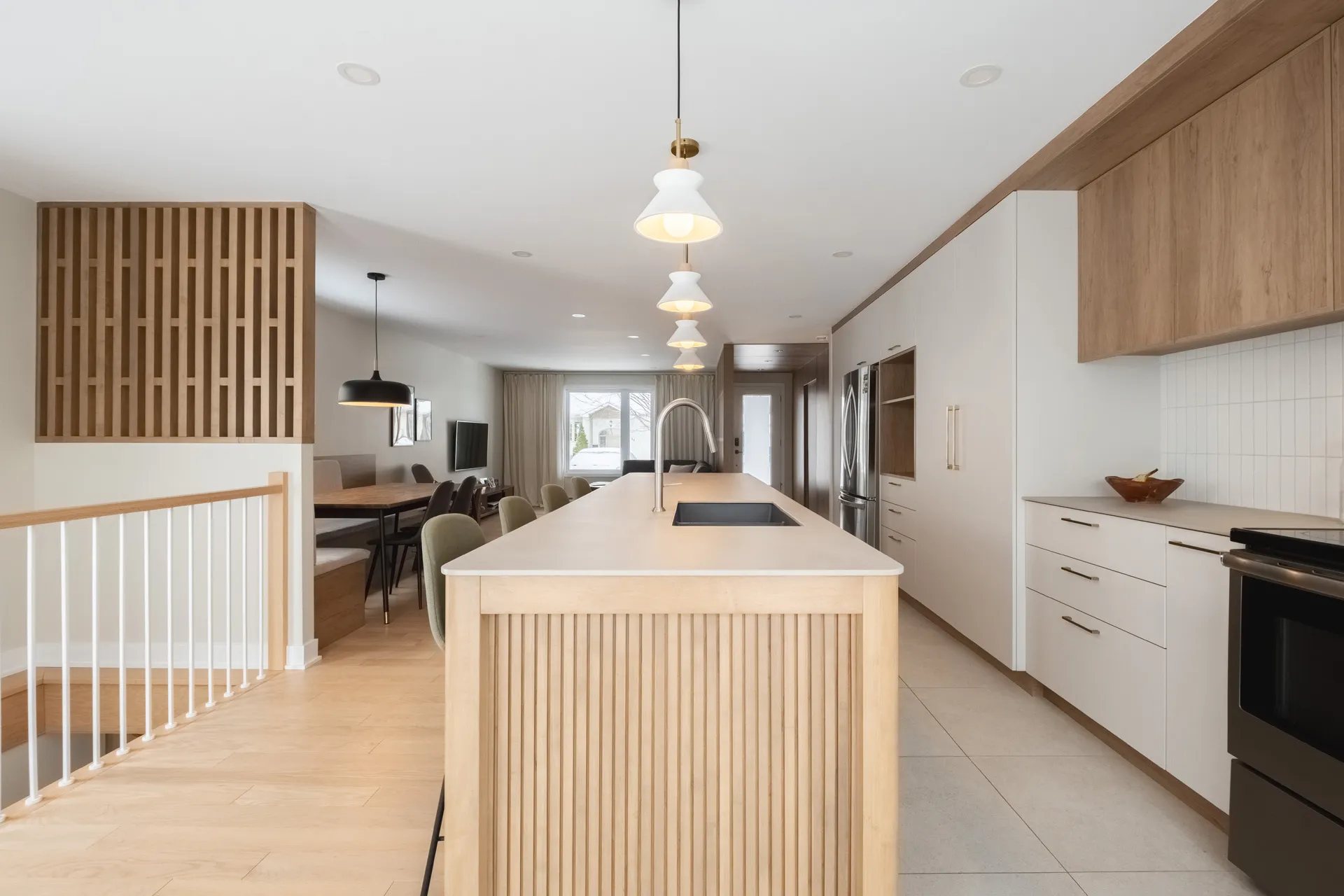 Cuisine moderne Léveillé avec armoires blanches et bois, îlot avec dosseret carrelé, comptoir blanc et luminaires suspendus.