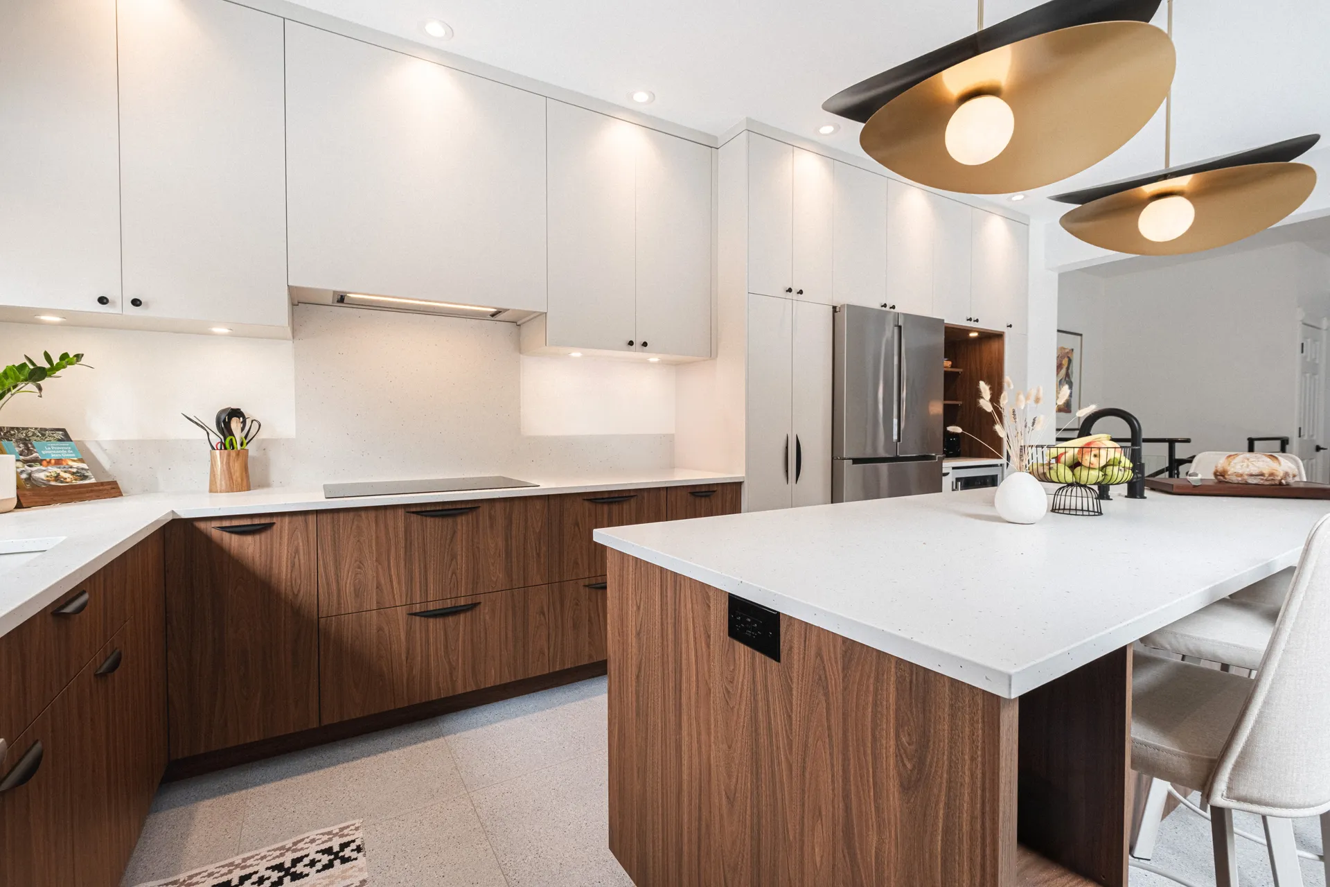 Cuisine moderne Menuitech avec armoires blanches et noyer, comptoir blanc, îlot central, dosseret blanc et luminaires suspendus dorés