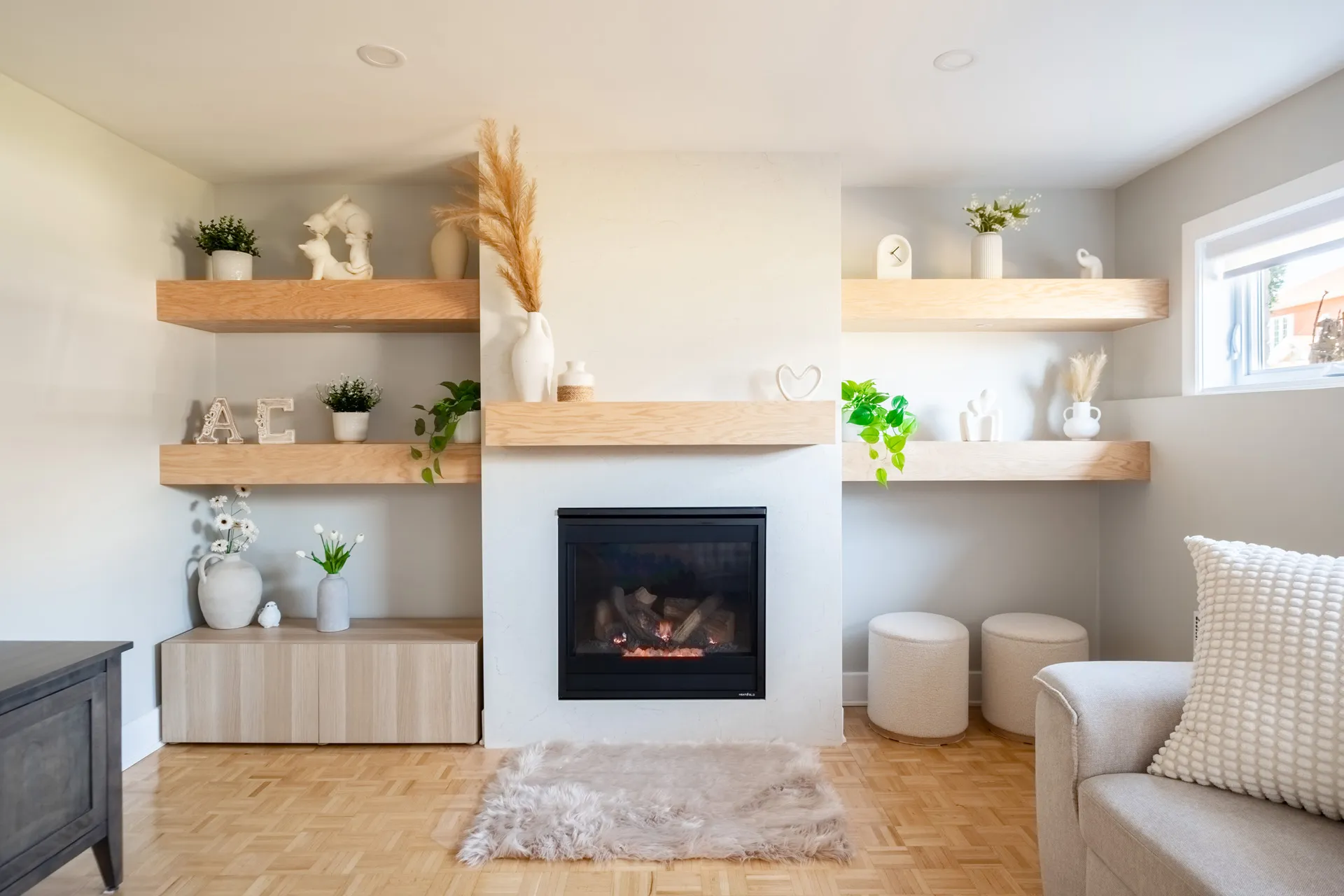 Salon moderne avec foyer encastré, murs blancs, étagères en bois clair, poufs beiges et décoration minimaliste
