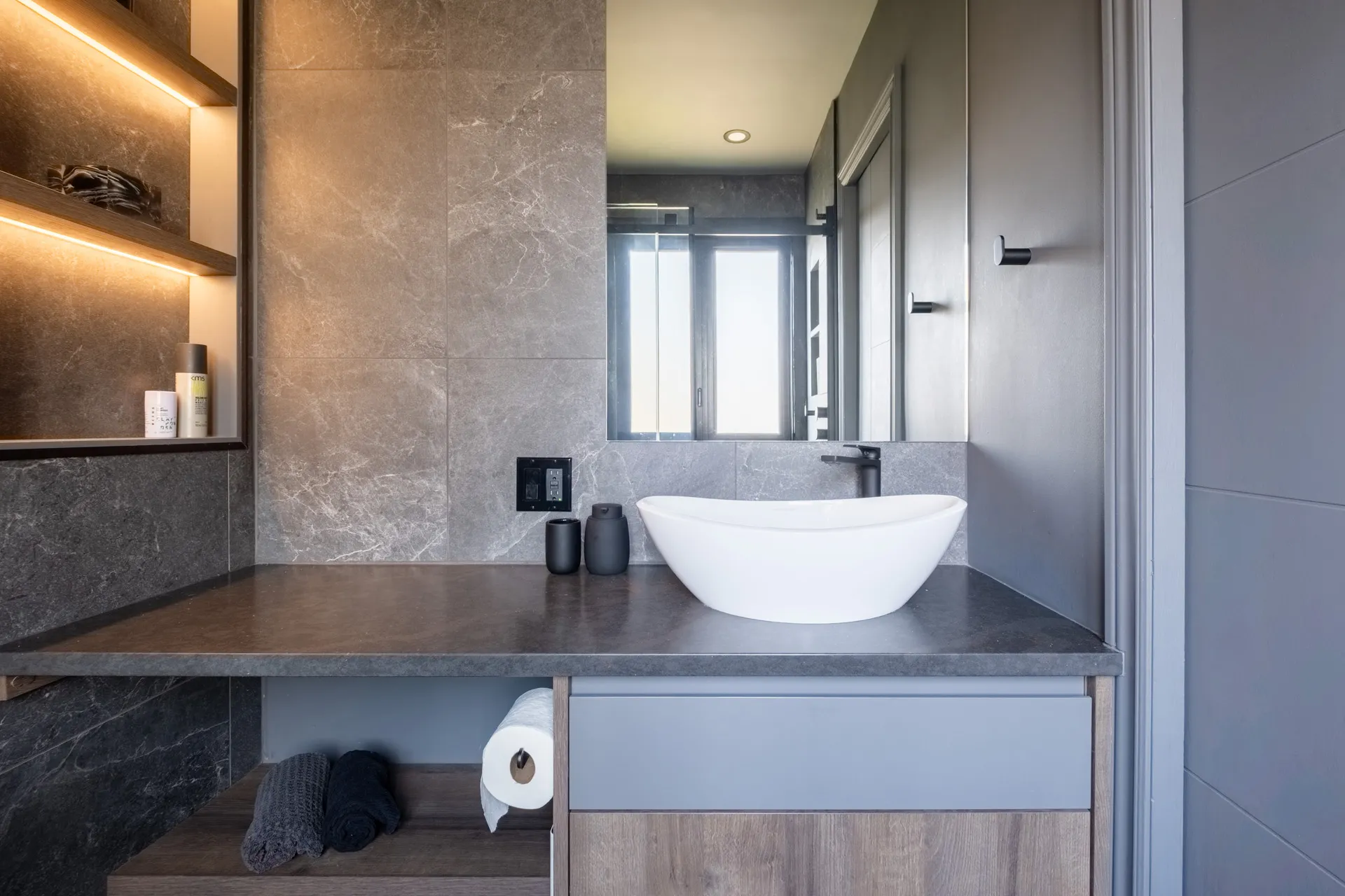 Salle de bain moderne Menuitech avec vanité grise, comptoir anthracite, lavabo blanc et éclairage intégré aux étagères
