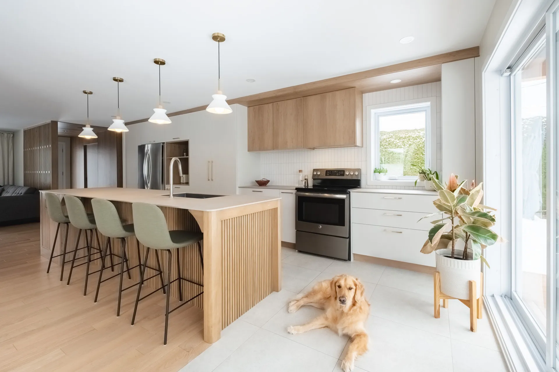 Cuisine moderne Blainville : armoires bois clair et blanches, îlot avec sièges verts, comptoir blanc, dosseret métro, luminaires laiton