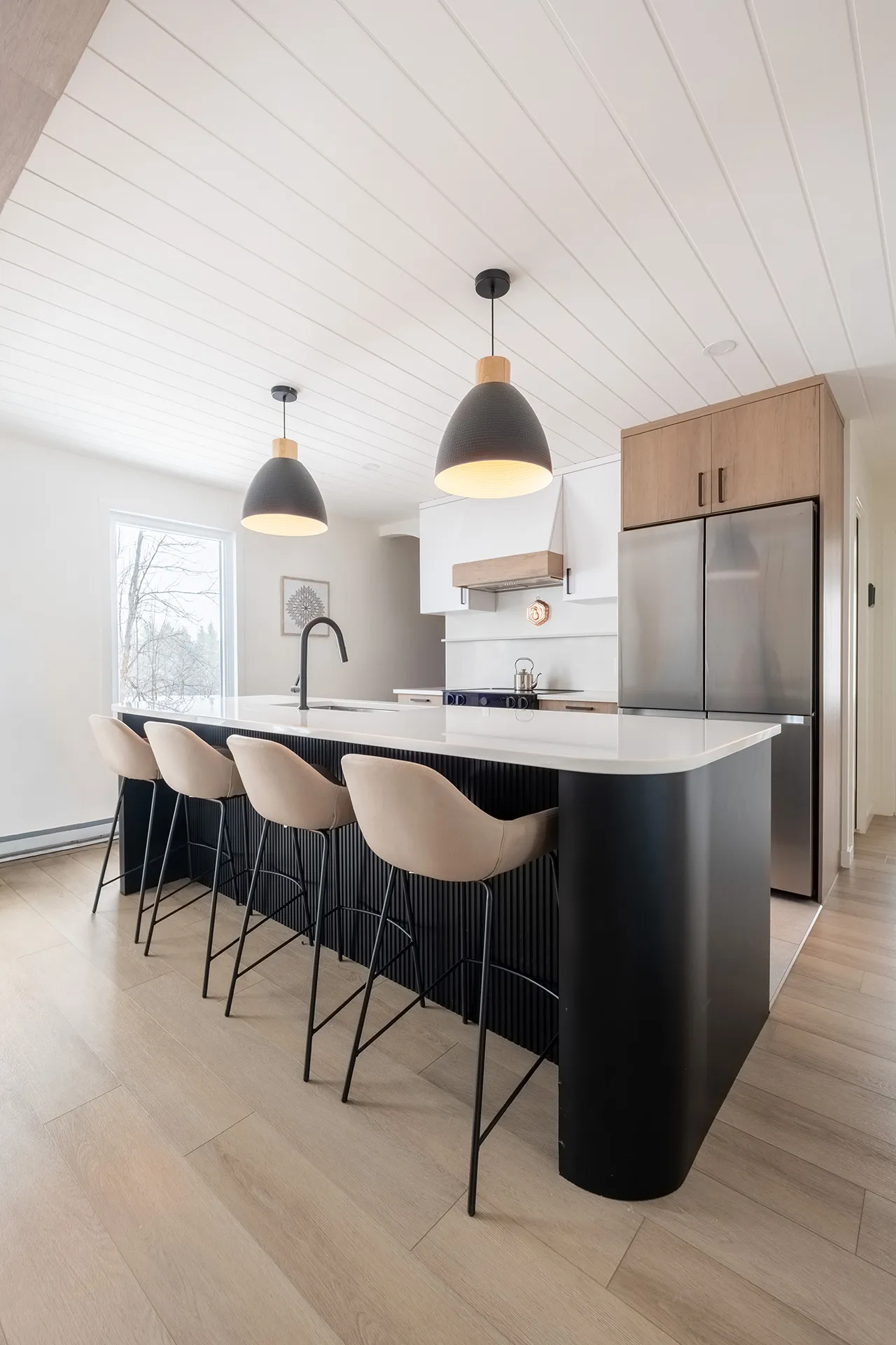 Cuisine moderne Alarie avec îlot noir, comptoir blanc, armoires blanches et bois clair, pendentifs noirs, tabourets beige