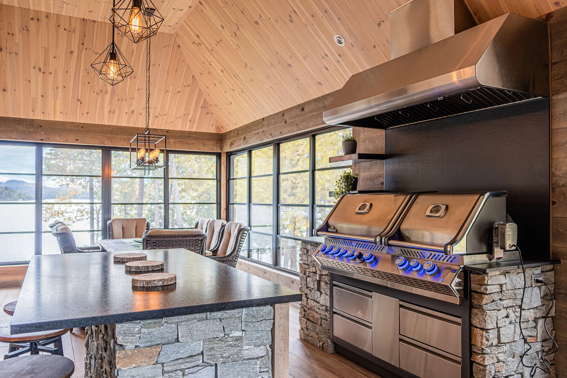 Outdoor kitchen with brown cabinets, black countertop, stone island, stainless steel grill and glulam wood ceiling