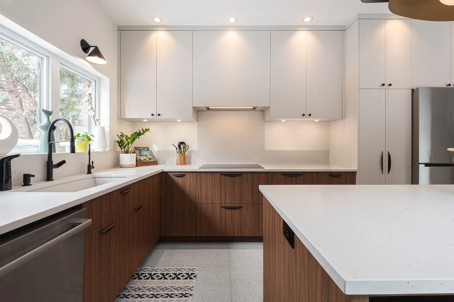Cuisine moderne Menuitech Sudan Montréal : armoires bois noyer et blanches, comptoir quartz blanc, îlot, dosseret beige clair