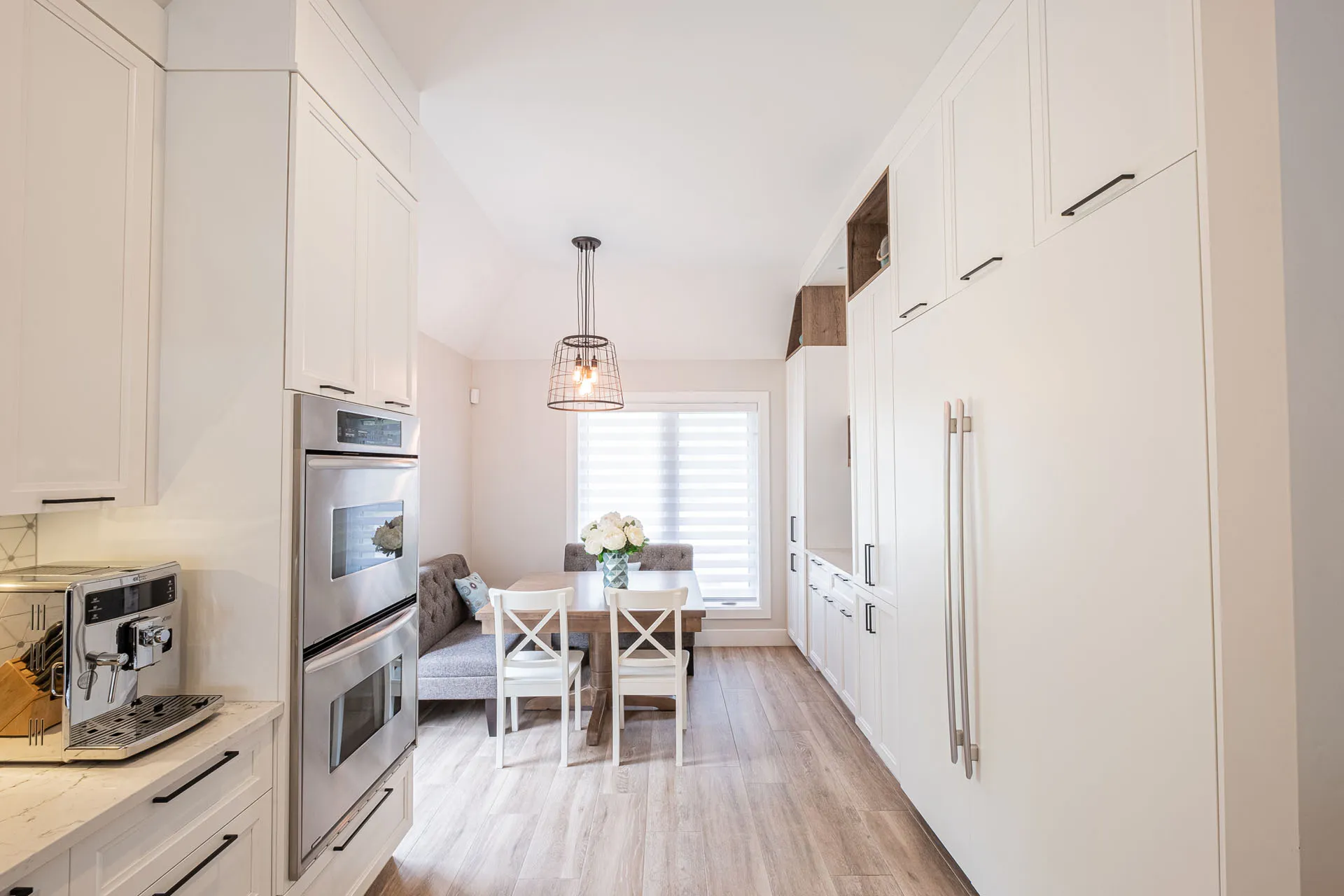 Modern white Simard kitchen with custom cabinets, light countertops, stainless steel appliances and pendant lighting.