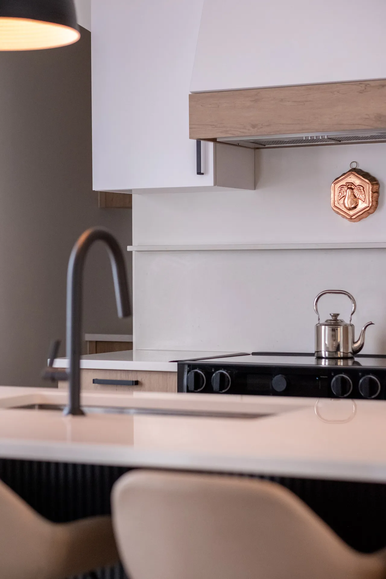 Cuisine moderne Alarie avec armoires blanches et bois, comptoir beige, îlot noir, dosseret blanc, luminaire suspendu