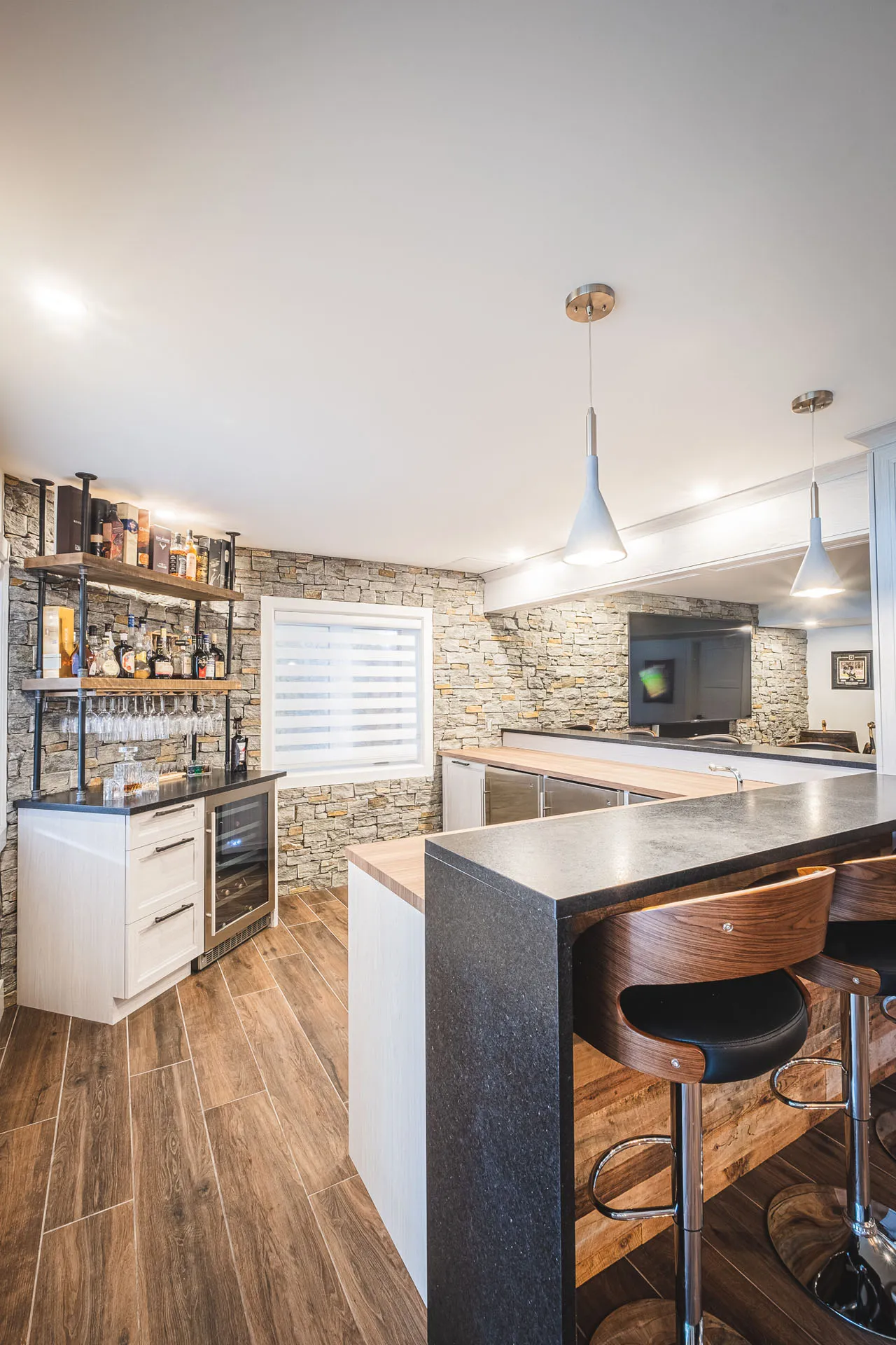Modern kitchen with white cabinetry, charcoal grey island, natural stone backsplash, blue pendant lights