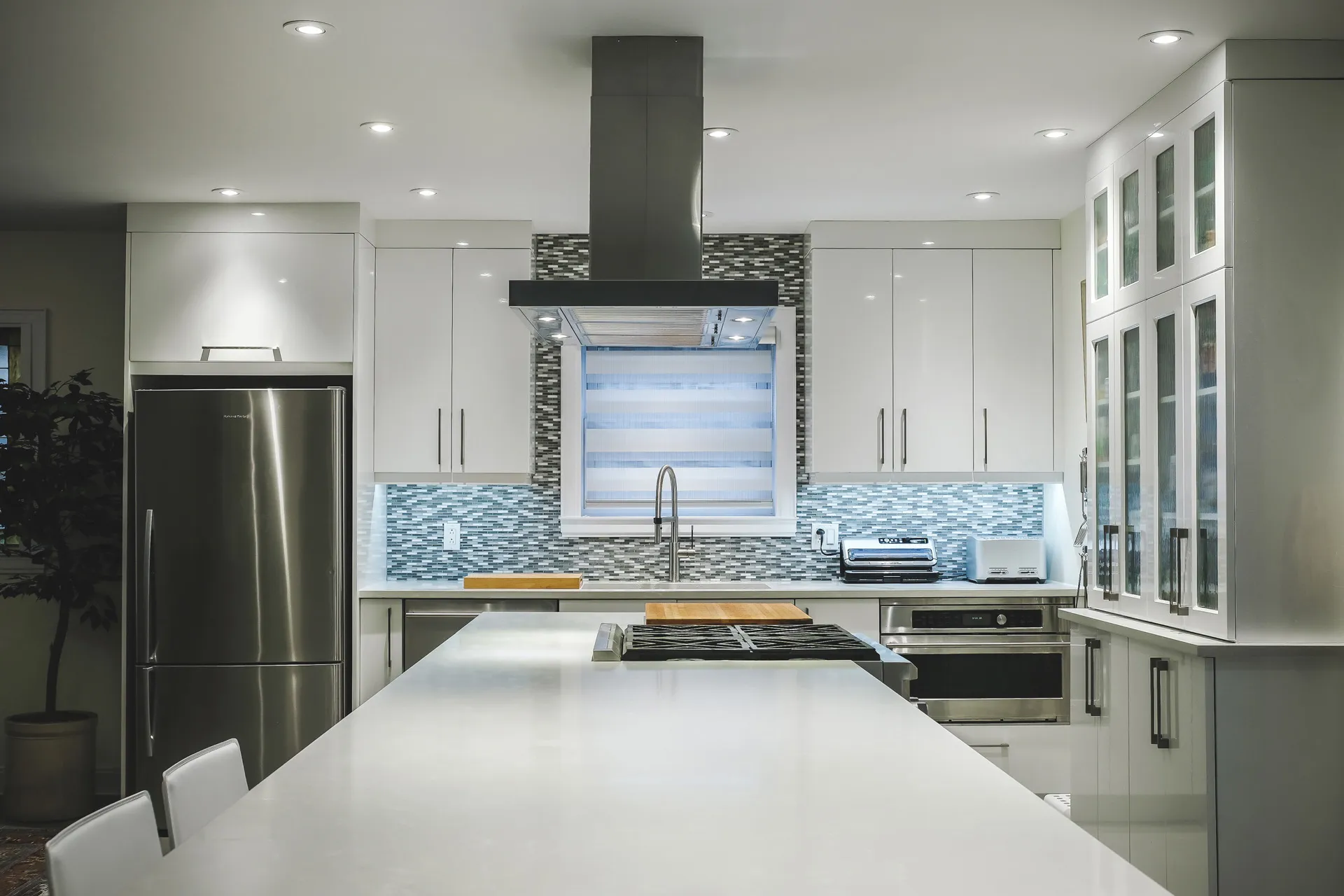 Modern Phaneuf kitchen with white cabinets, white countertop, blue-gray tile backsplash, island and black range hood