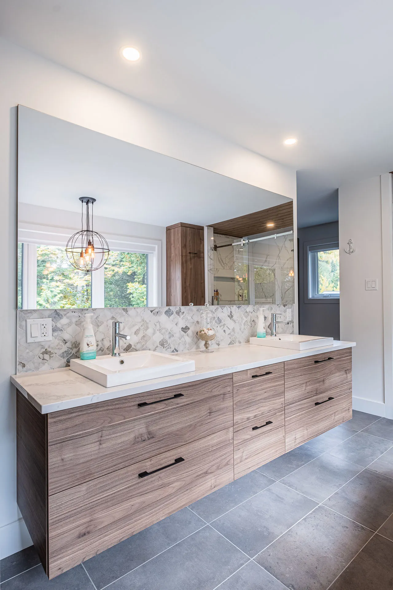 Modern bathroom with light wood double vanity, white countertop, herringbone marble backsplash and wall mirror