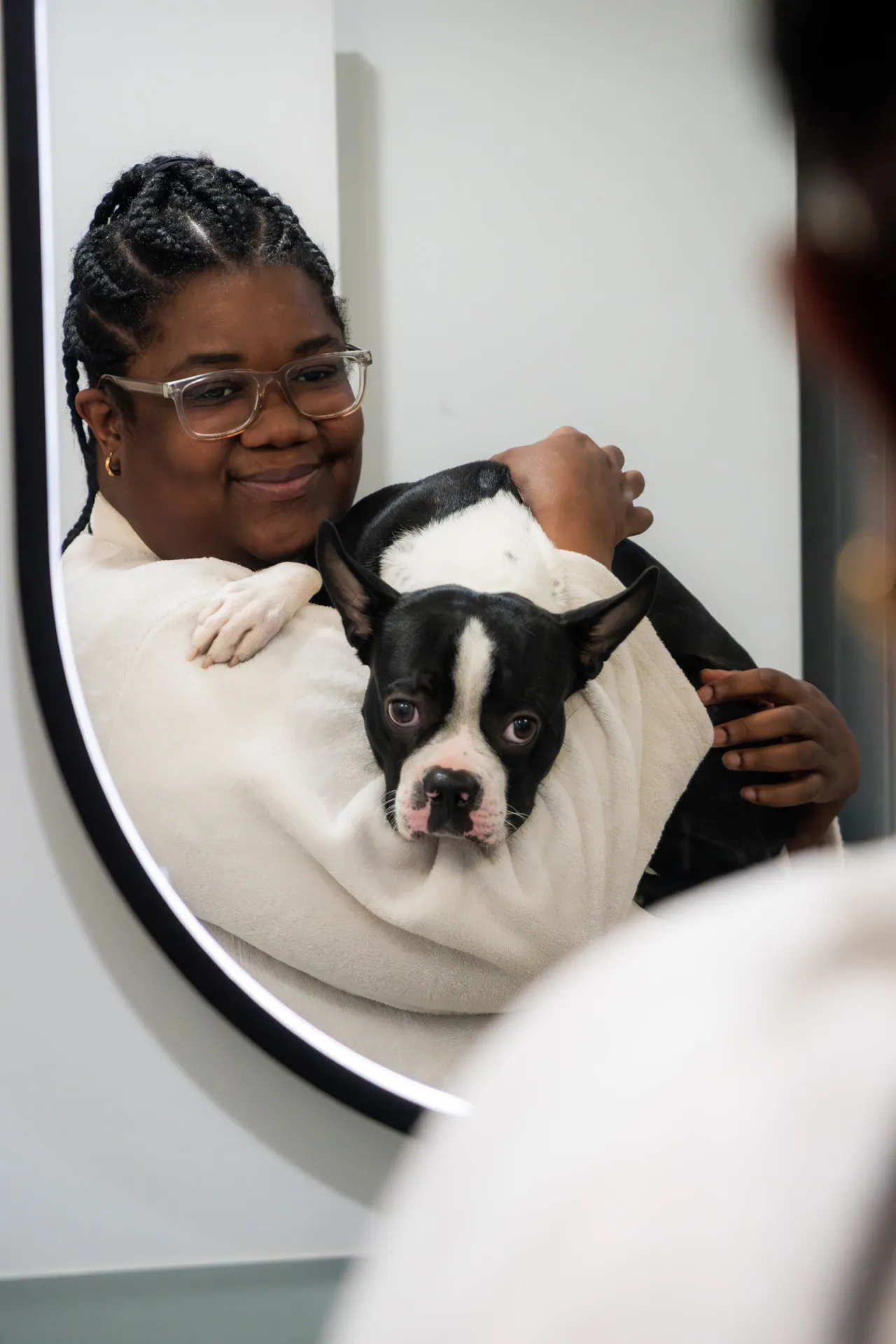 Jeune femme souriante avec lunettes tenant un chien noir et blanc devant un miroir