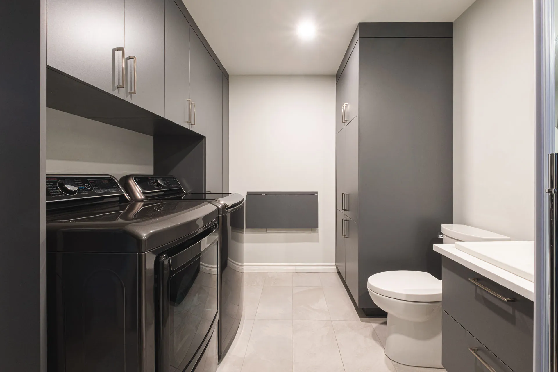 Gray and white bathroom with gray cabinets, white countertop, toilet and double sink by Menuitech