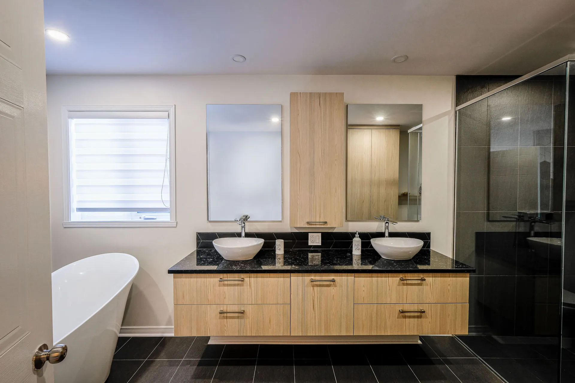Landry bathroom with natural wood vanity, black granite countertop, dual white vessel sinks and framed mirrors