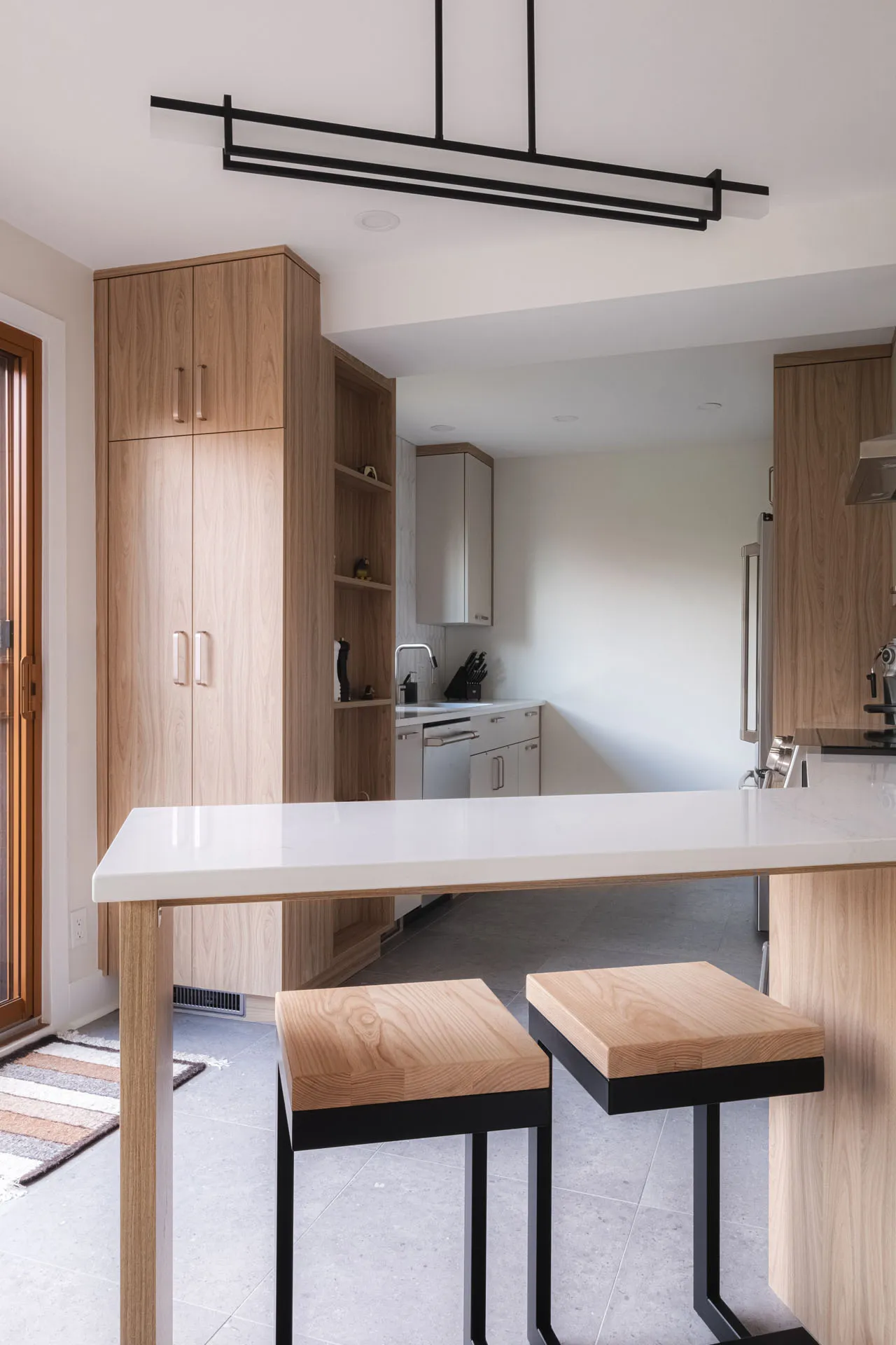 Menuitech renovated kitchen with light wood cabinets, white countertop, island with stools, suspended black pendant light.