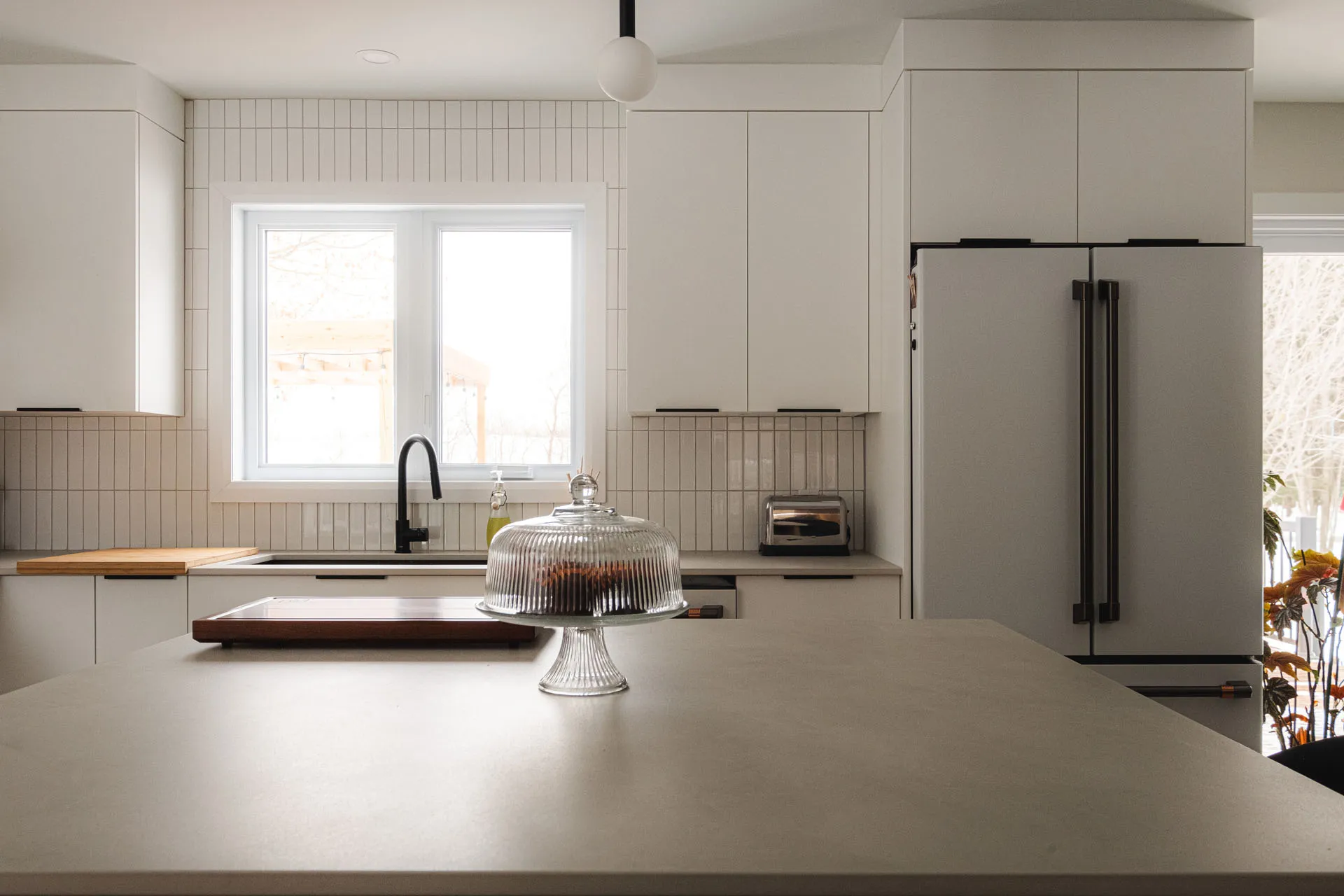 Robitaille kitchen Epiphany: cream white cabinets, light gray countertop, island, vertical tile backsplash, stainless steel appliances