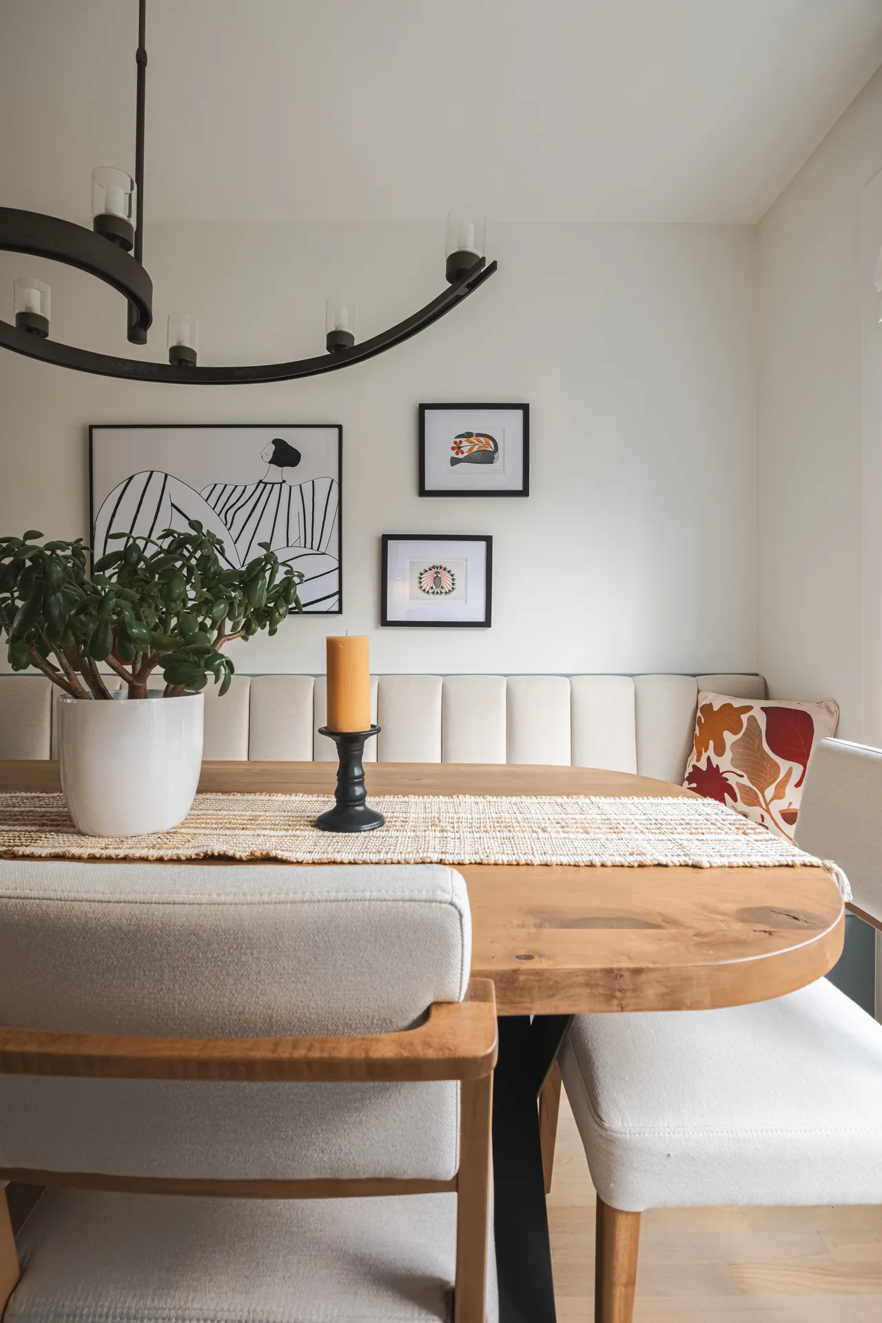 Salle à manger moderne avec banquette beige, table bois clair, lustre noir arqué et cadres muraux minimalistes