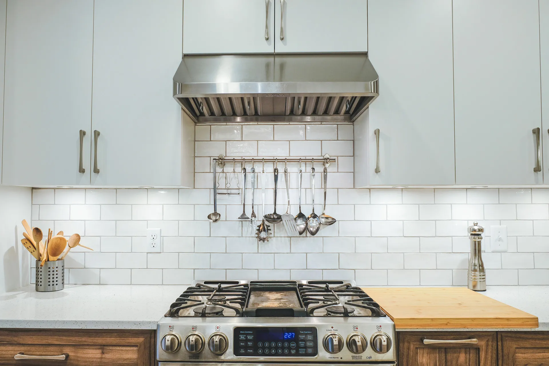 White kitchen with Menuitech cabinets, grey countertop, white subway backsplash, stainless steel range and hood, wooden island.