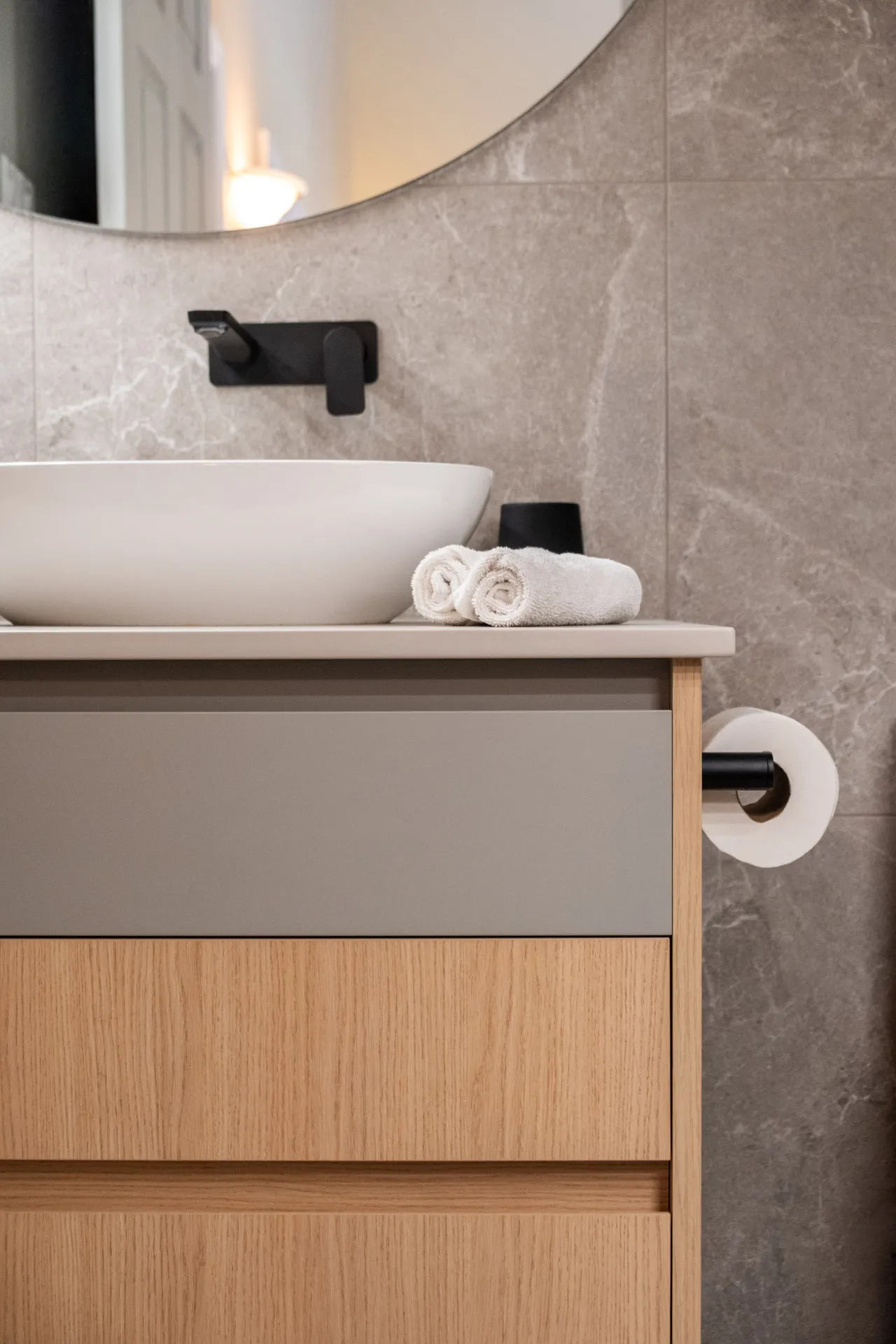 Salle de bain Garraud : vanité bois et gris, comptoir blanc, dosseret pierre grise, robinetterie noire