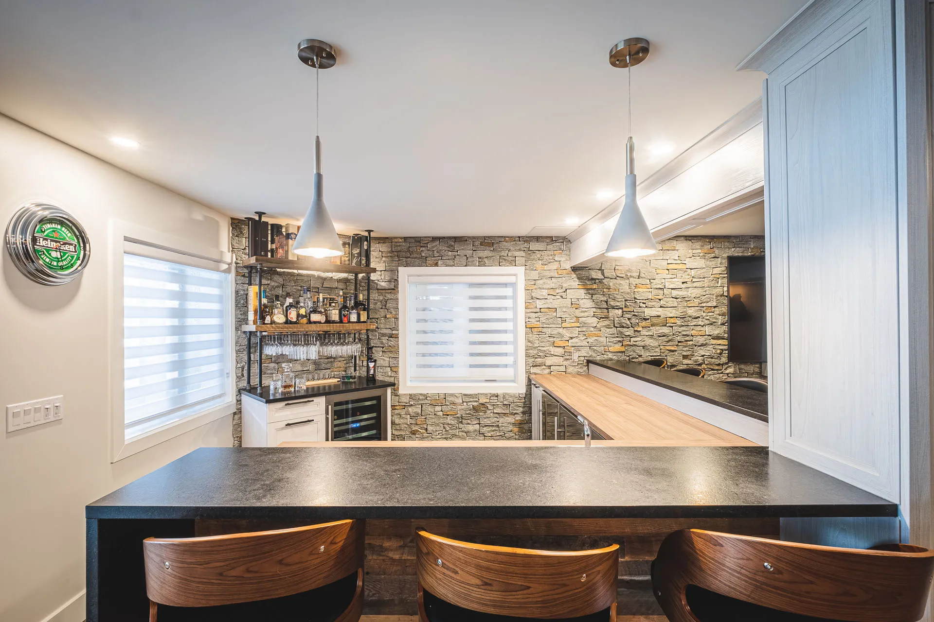 Modern residential bar with black island, gray countertop, white cabinetry, stone backsplash and pendant lighting