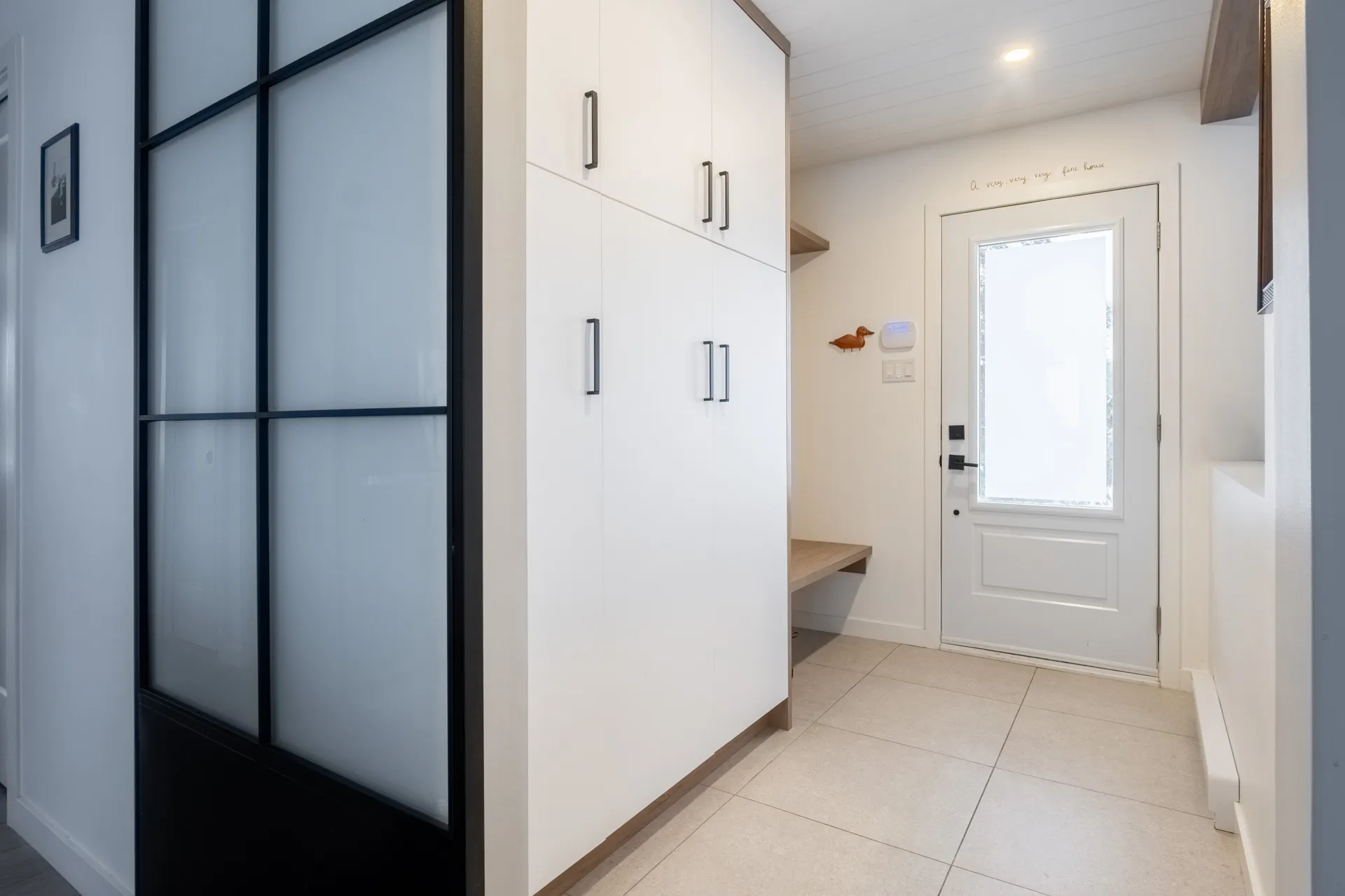 Entrée avec armoires blanches sur mesure, comptoir bois clair, porte vitrée et rangements muraux Menuitech