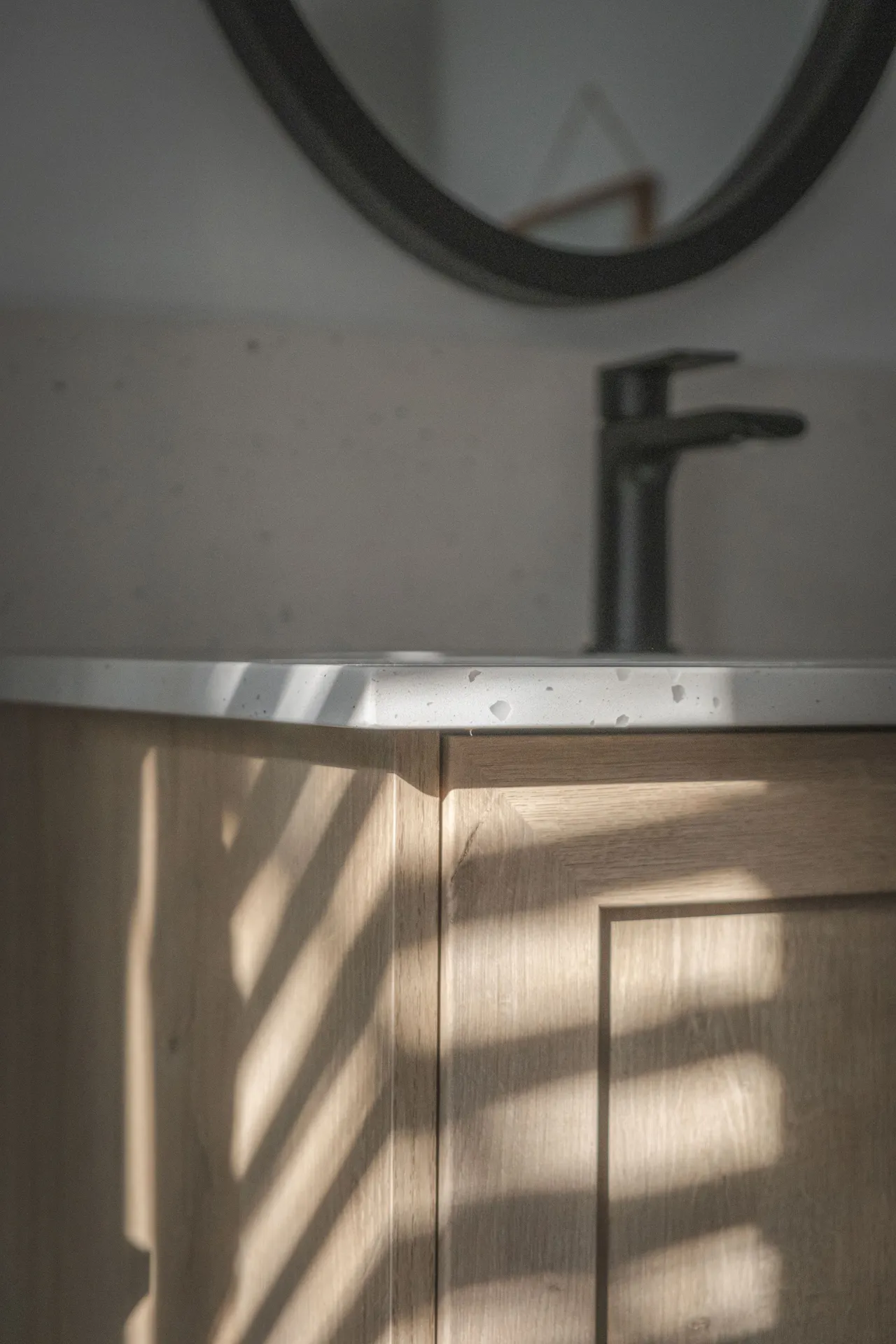 Salle de bain Diamant Blainville : vanité bois clair, comptoir blanc, robinet noir, miroir rond, luminosité naturelle