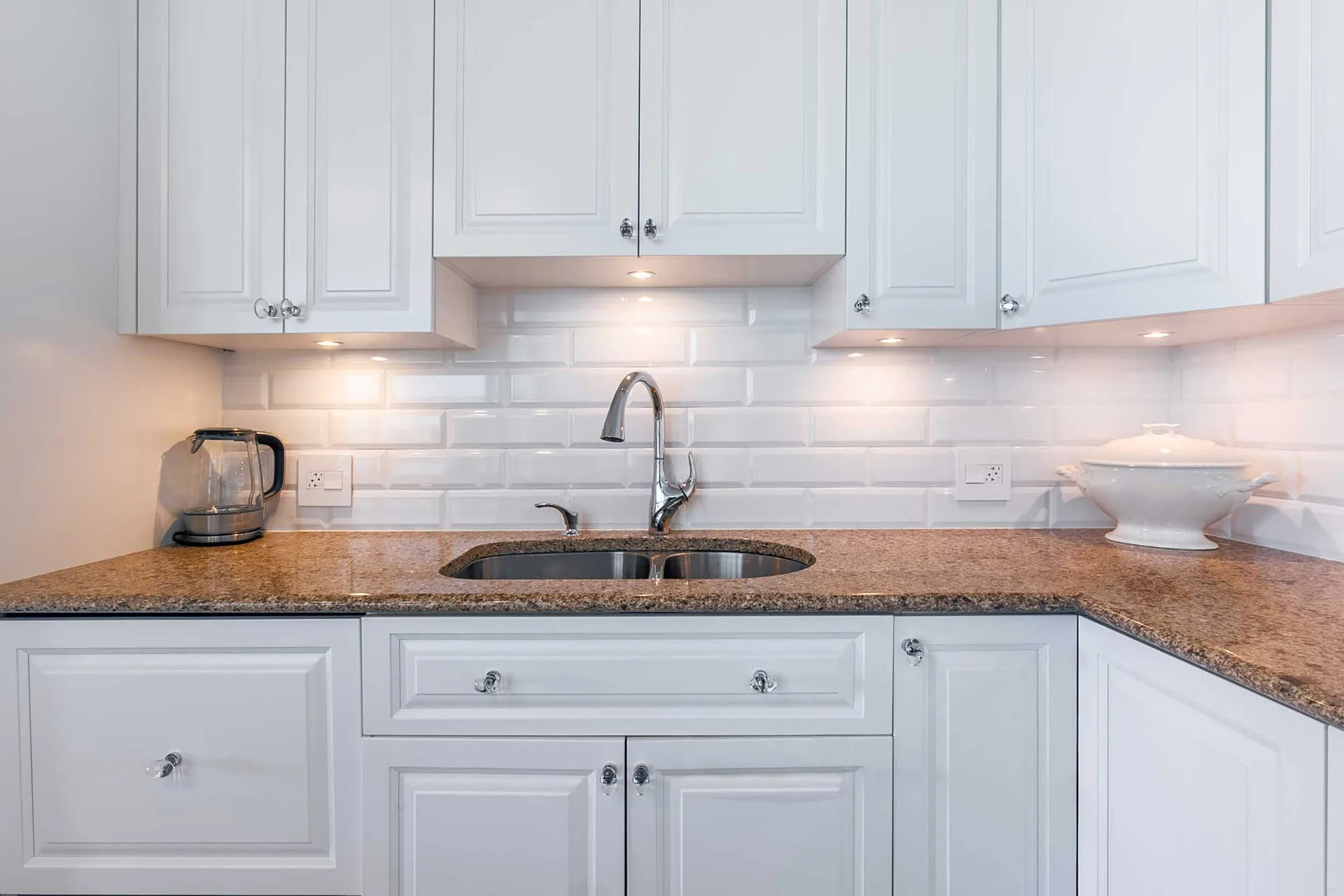 White Menuitech kitchen with granite countertop, white subway backsplash, custom cabinets and under-cabinet lighting