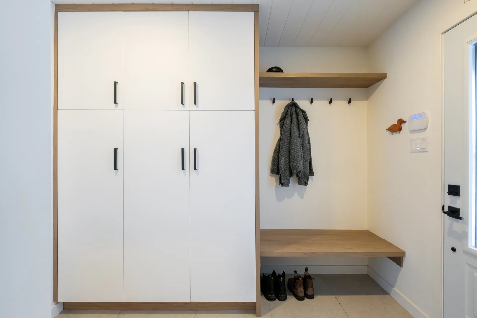 Entrée moderne Menuitech : armoires blanches, comptoir bois, crochets muraux et étagère flottante