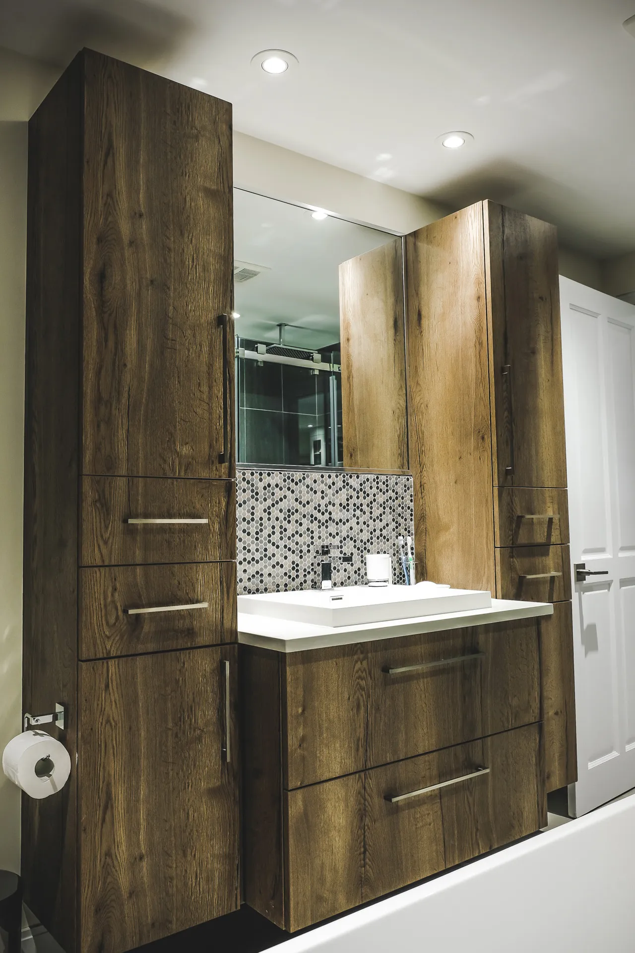 Phaneuf bathroom: dark wood cabinets, white countertop, grey mosaic backsplash, large mirror, recessed lighting