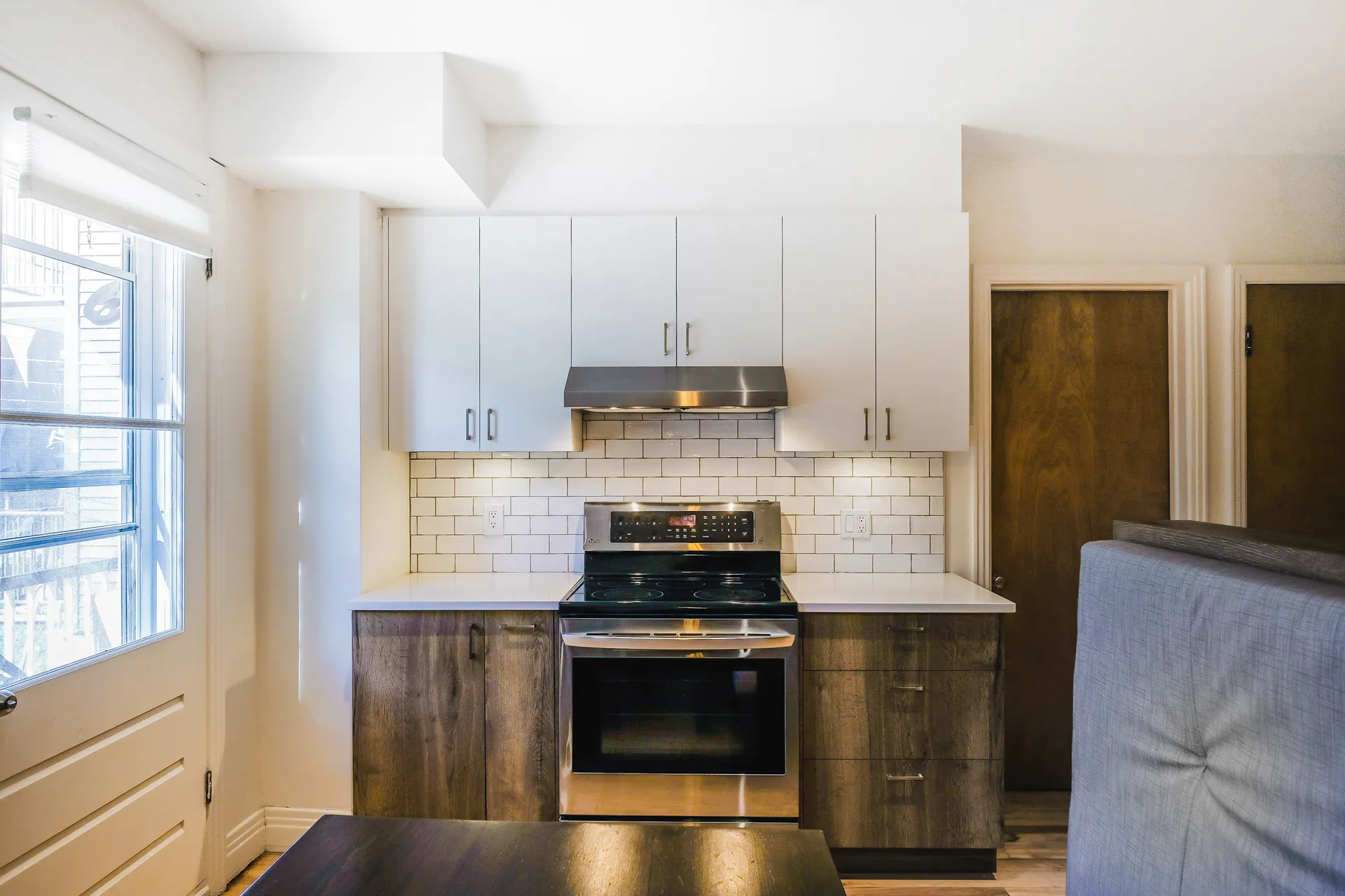 Menuitech renovated kitchen featuring white and dark wood cabinets, white countertop, white subway tile backsplash, island and stainless steel appliances.