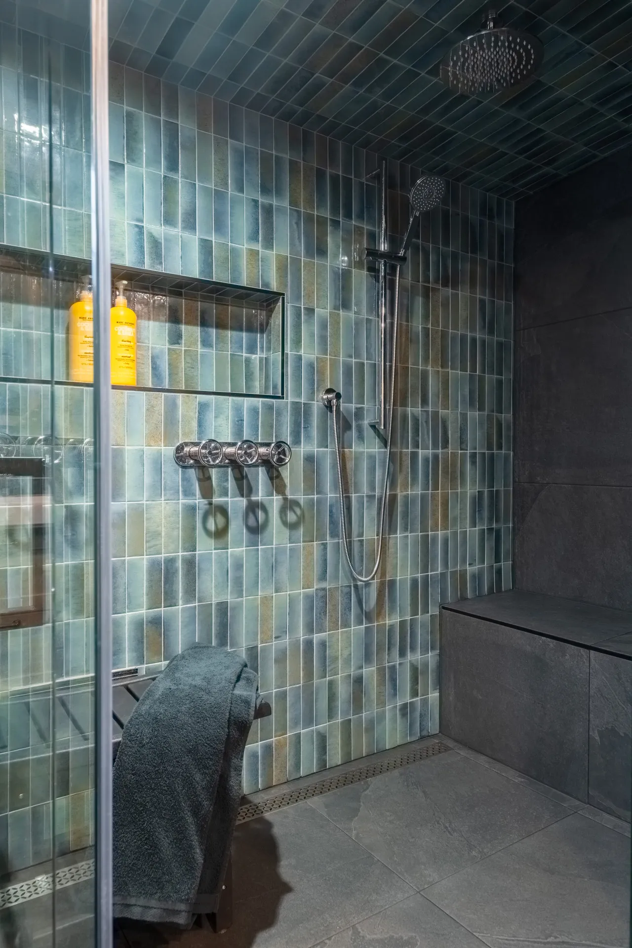 Modern shower with gradient green tile, chrome fixtures, rainfall showerhead and gray towel bar