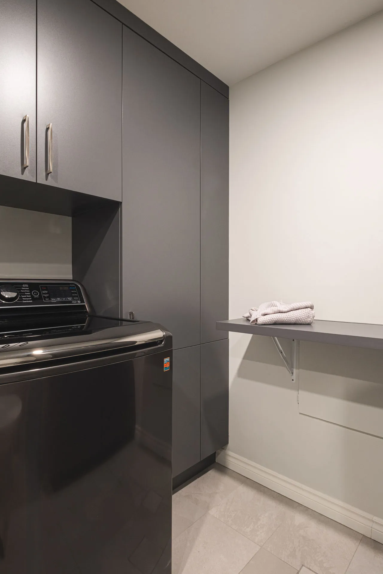 Grey laundry room with custom cabinets, black washer and white folding ironing table